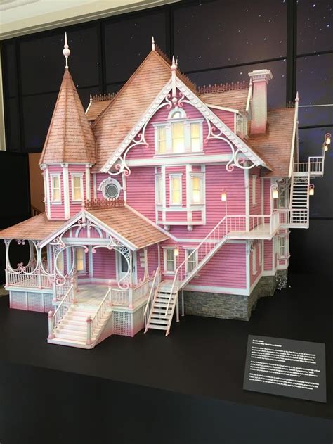 a pink doll house on display in front of a black wall with stairs and windows