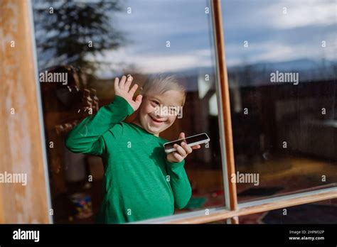 Happy little boy with Down syndrome using smartphone and waving through window Stock Photo - Alamy