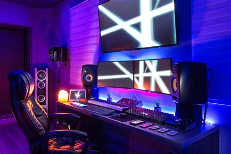 a computer desk with two monitors and speakers in front of purple lighting on the wall