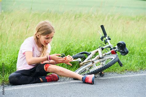 Sad crying little child girl fell from the bike in the summer park. Bleeding on hands and feet ...