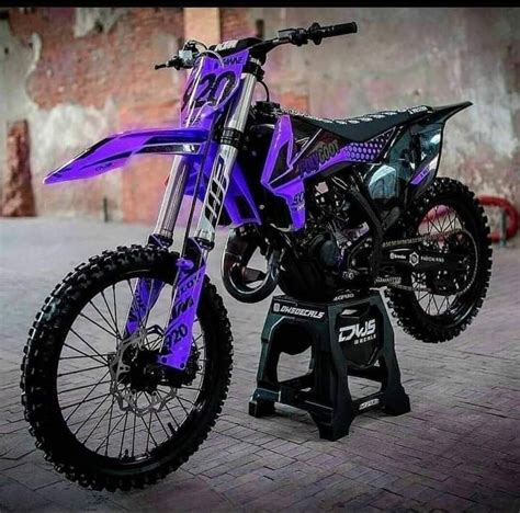 a purple and black dirt bike parked on top of a brick floor next to a wall