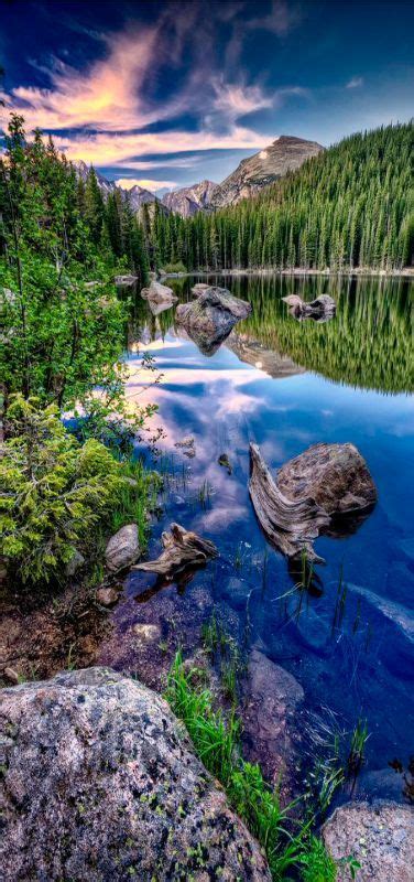 a lake surrounded by trees and rocks under a cloudy sky