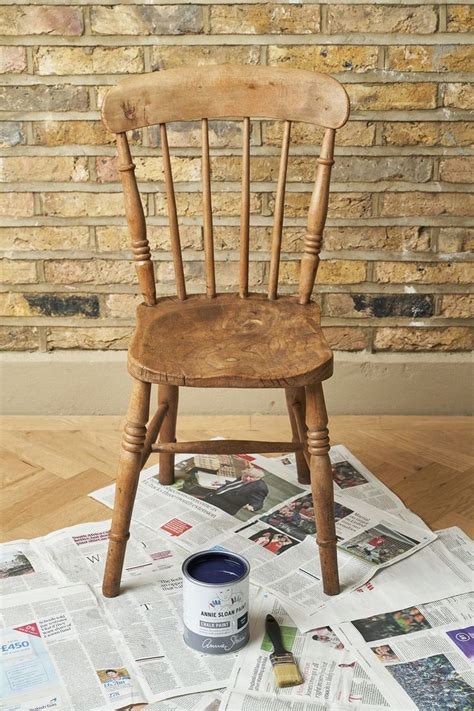 a wooden chair sitting on top of a pile of newspaper next to a paint can