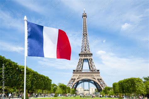 French flag flying in bright blue sky above the Eiffel Tower in Paris ...