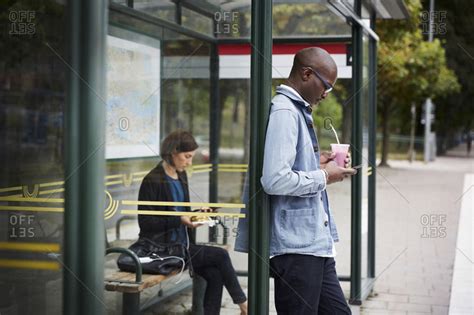 Mid adult commuters waiting at bus stop in city stock photo - OFFSET