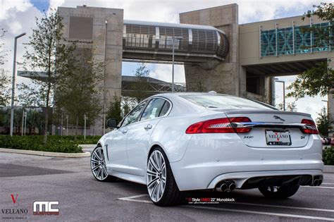 the rear end of a white car parked in a parking lot near a large building