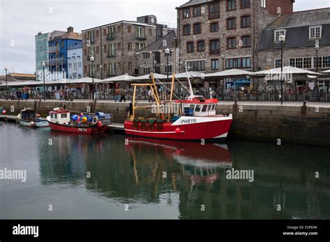 fishing boats moored in the Sutton harbour, Plymouth, UK with the shops ...