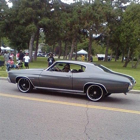 an old car driving down the road with people in the back seat and onlookers