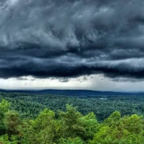 the sky is filled with dark clouds and green trees