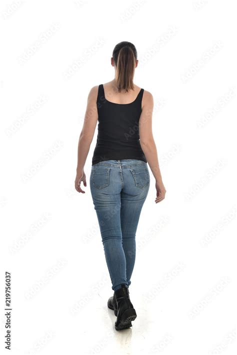 full length portrait of brunette girl wearing black single and jeans. standing pose with back to ...