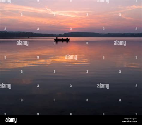 Lake sunset with fisherman fishing from boat Stock Photo - Alamy