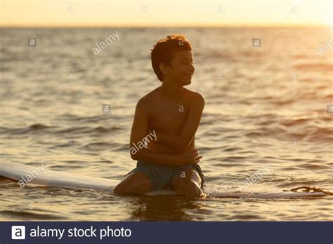 Download this stock image: Surfer sitting on a surfboard at dawn - boy - in swimming shorts ...