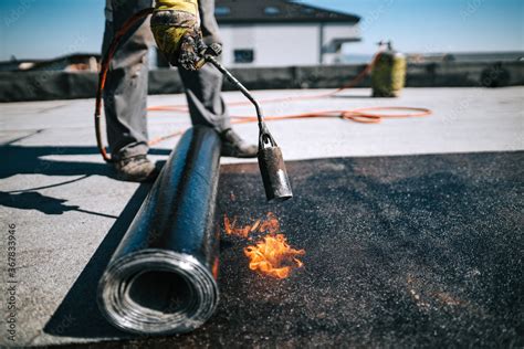 Professional workers insulating rooftop with bitumen membrane ...