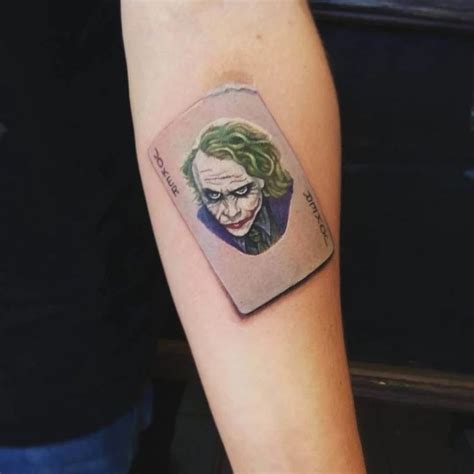 a joker tattoo on the left arm with a card in it's middle sleeve