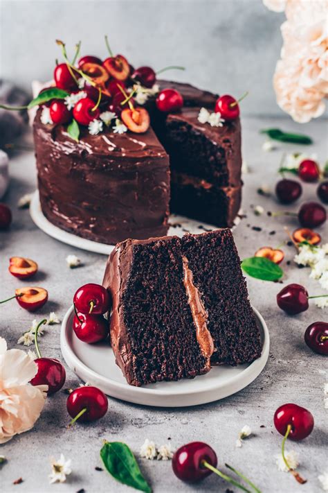 two slices of chocolate cake on plates with cherries