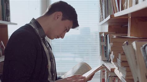 Young caucasian man standing at bookshelf in library, looking through book flipping and turning ...