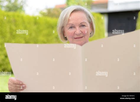 Elderly Woman Sitting In The Park While Holding A Blank Big Ocher Paper