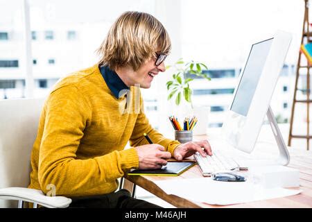 Hipster Smiling While Using Graphics Tablet At Computer Desk Stock