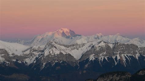 Landscape View Of Snow Capped Rock Mountains In Light Pink Orange Sky