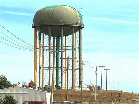 Two Cars Are Parked In Front Of A Large Water Tower On The Side Of A Road