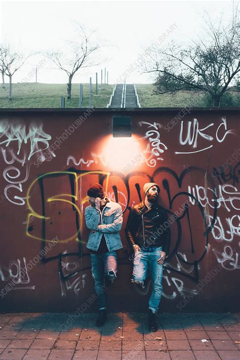 Portrait Of Two Male Hipsters Leaning Against Graffiti Wall Stock