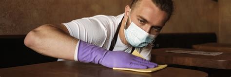 A Man Waiter In A Protective Mask Wiping A Table In A Cafe Stock Photo