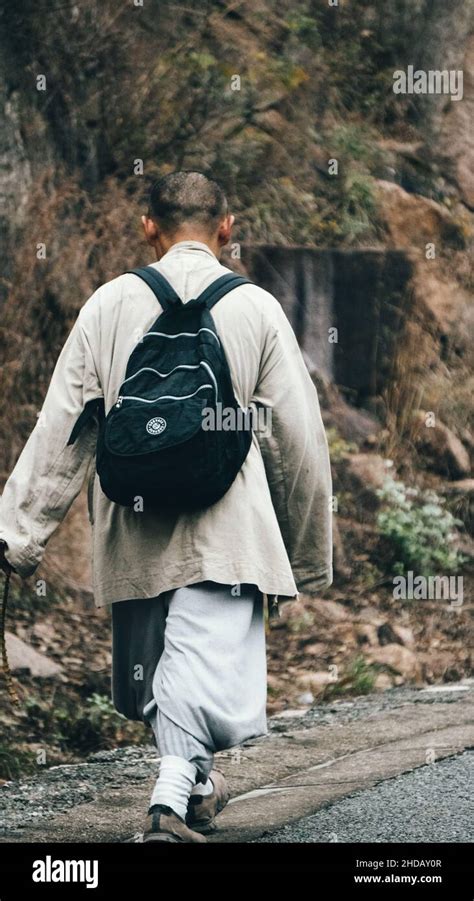 Vertical Back View Of A Monk With A Backpack Walking In A Park Stock