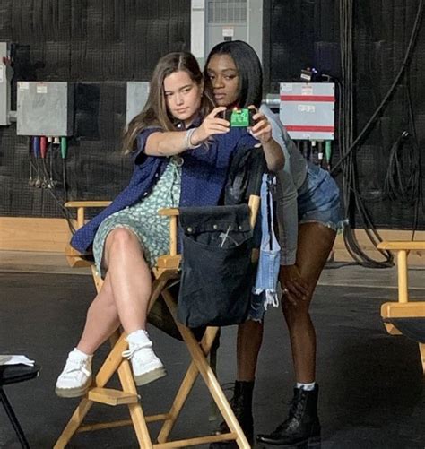 Two Women Sitting In Chairs Taking Pictures With Their Cell Phones