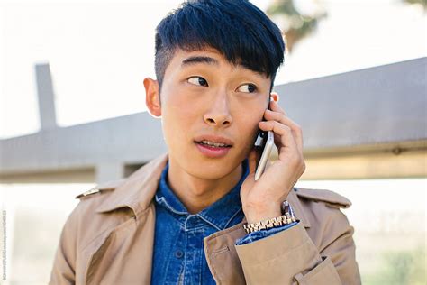 Stylish Young Asian Man Using A Mobile Phone In The Street Del Colaborador De Stocksy