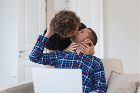 Pareja gay ovely besándose mientras está sentado en su sala de estar en casa dos románticos