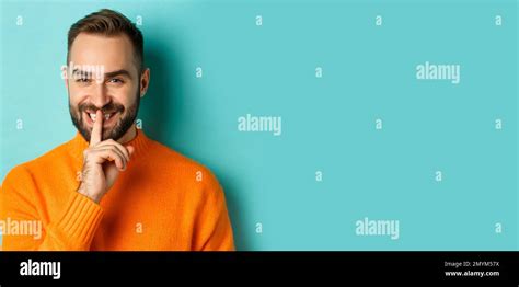 Close-up of handsome smiling man hushing, telling secret, standing over ...