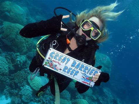 A Woman Scubas In The Ocean Holding A Sign That Says Great Barrier Reef