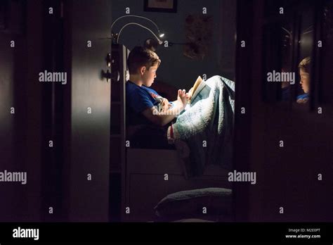 Caucasian boy reading book in bed at night Stock Photo - Alamy