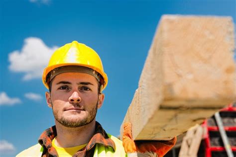 Un Ouvrier De La Construction Qui Porte Une Poutre En Bois Photo Premium