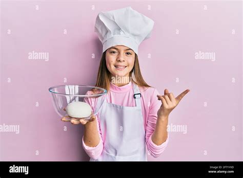 Belle petite fille brunette portant un chapeau de chef tenant la pâte à pain sourire heureux
