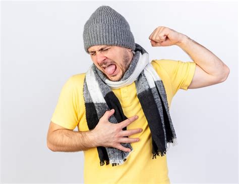 Ennuyé jeune homme malade blonde portant chapeau d hiver et écharpe tend les biceps met la main