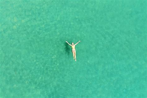 La vista superior de una mujer joven en un bikini brillante está nadando en el mar azul