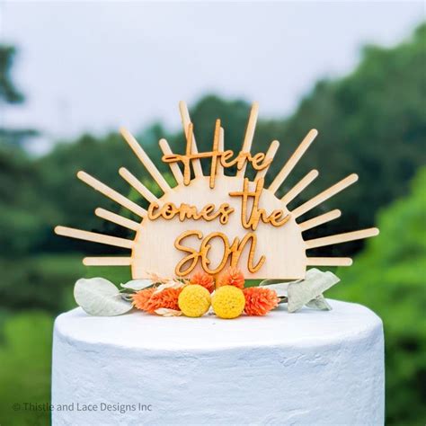 A Cake Topper With The Words Here Comes The M On It And Flowers