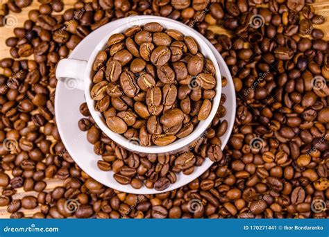 White Cup Filled With Coffee Beans On Wooden Table Top View Stock