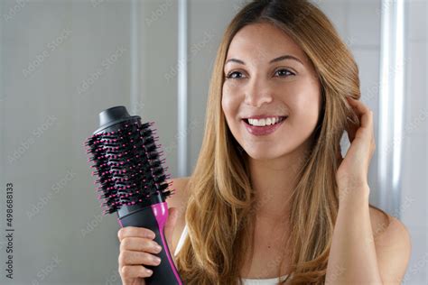 Pleased Girl Holds Round Brush Hair Dryer To Style Hair In Her Bathroom At Home Young Woman