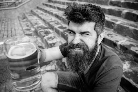 Man With Beard And Mustache Holds Glass With Beer While Sits On Stone