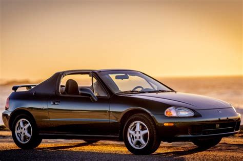 A Black Sports Car Parked On The Beach At Sunset