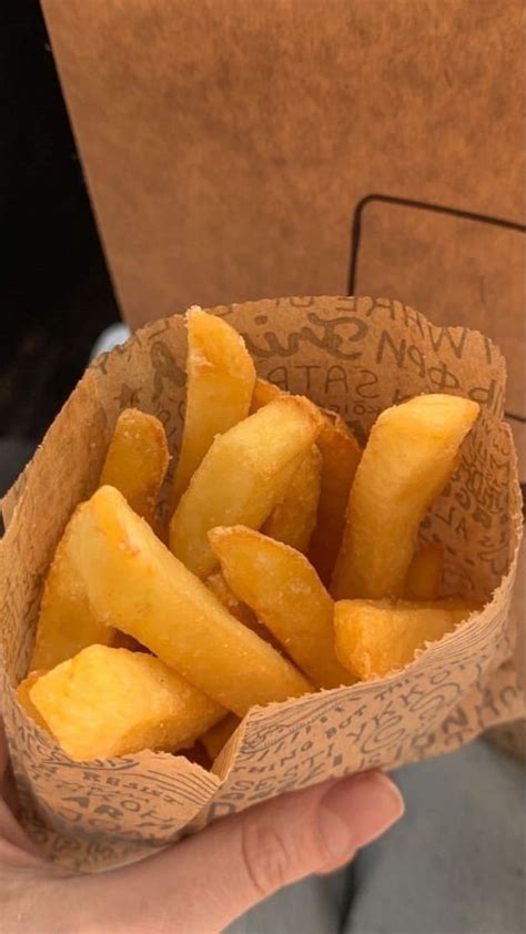 A Hand Holding A Paper Container Filled With French Fries