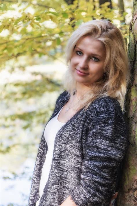Portret Van Het Glimlachen Het Blonde Jonge Vrouw Leunen Tegen Een Boom Stock Foto Image Of