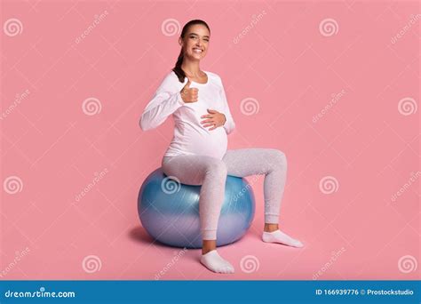 Pregnant Girl Sitting On Fitball Gesturing Thumbs Up Over Pink