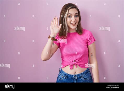 Blonde Caucasian Woman Standing Over Pink Background Waiving Saying Hello Happy And Smiling