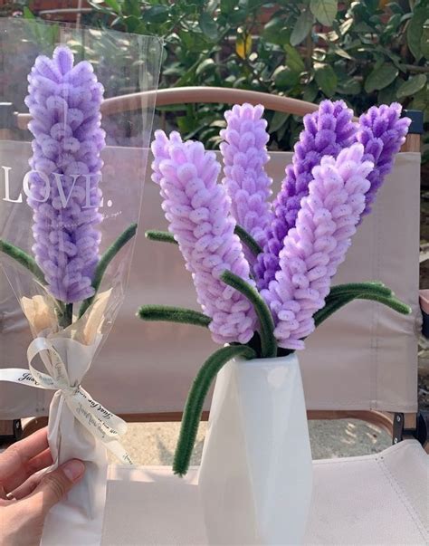 Purple Flowers Are In A White Vase On A Table Next To A Person S Hand