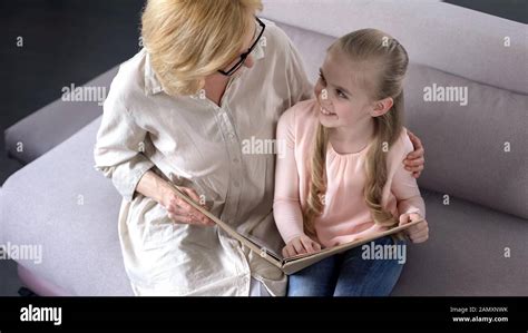 Smiling Little Female Child Reading Book With Her Elderly Nanny Care