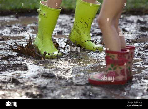 Children Jumping In A Muddy Puddle Wearing Wellington Boots Stock