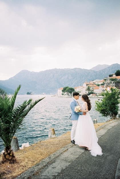 Premium Photo Bride And Groom Stand Hugging On The Embankment Of